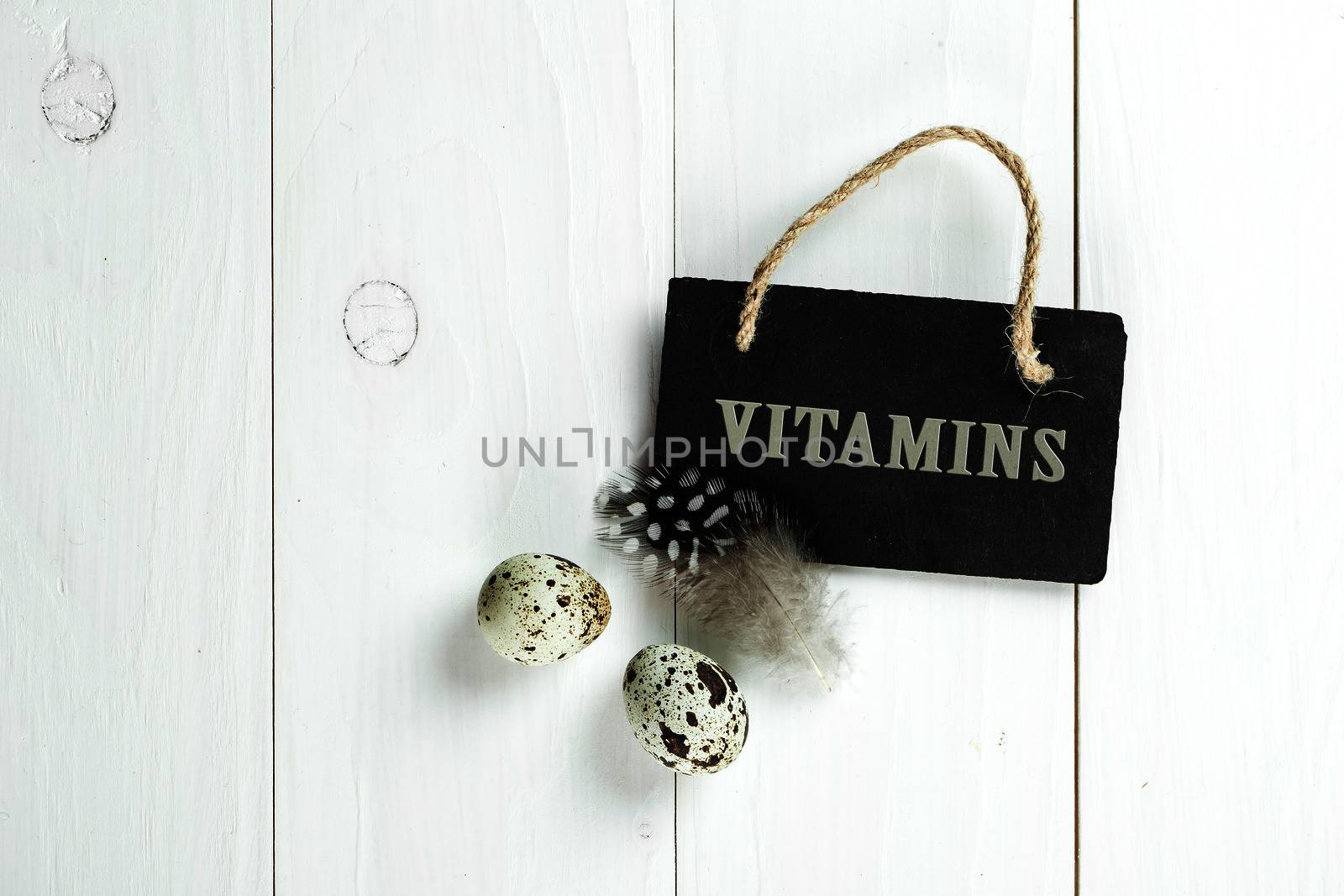 Quail eggs and feather with vintage blackboard on white wooden background, with copy space for greeting text.