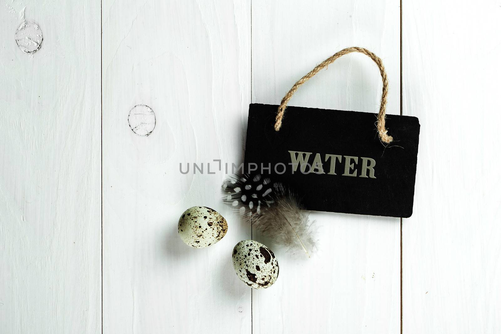 Quail eggs and feather with vintage blackboard on white wooden background, with copy space for greeting text.