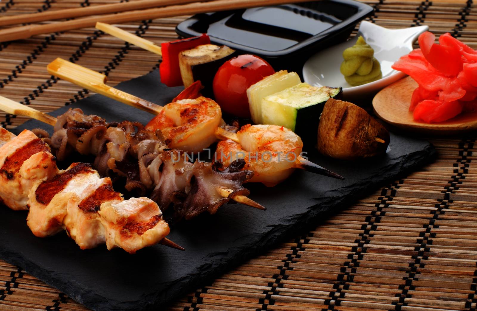 Grilled Salmon, Octopuses, Shrimps and Vegetables on Wooden Stick with Ginger, Soy Sauce and Wasabi closeup on Straw Mat background