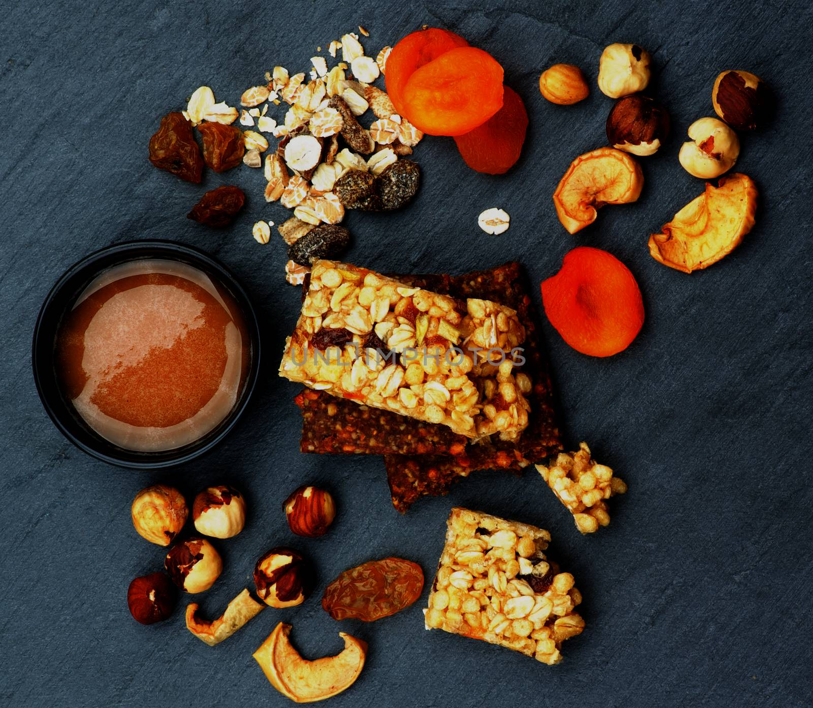 Arrangement of Useful Granola Bars with Muesli, Nuts, Dried Apricots and Bowl of Honey closeup on Black Stone background. Top View