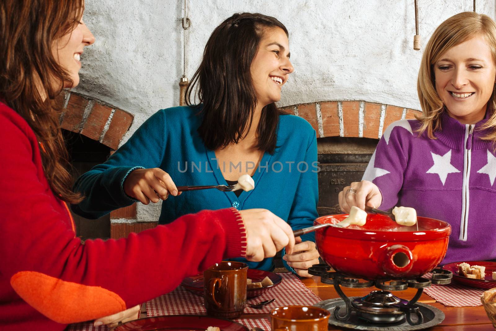 Photo of three beautiful females dipping bread into the melted cheese in a fondue pot.