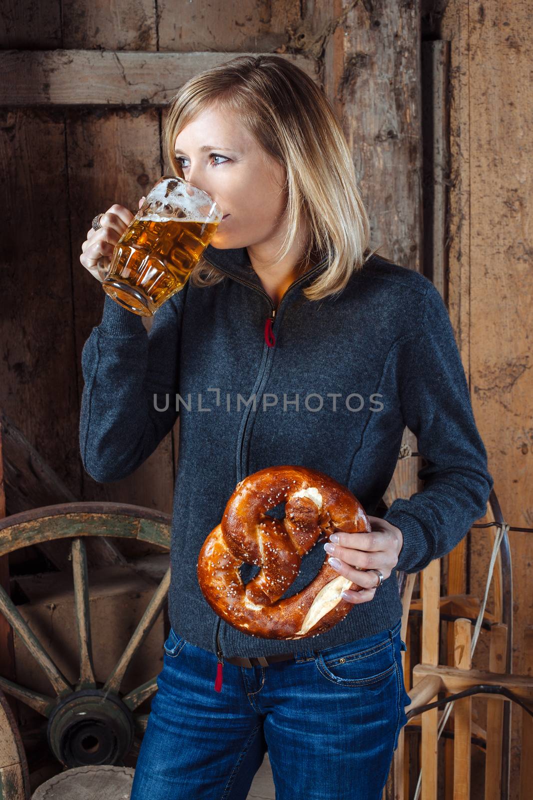 Photo of a beautiful blond woman eating and drinking a beer and pretzel inside an old barn.