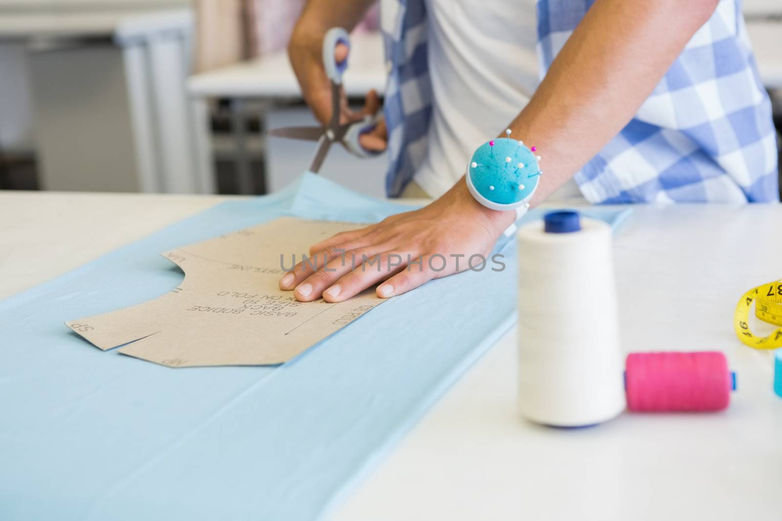 Fashion student cutting fabric with pair of scissors at the college