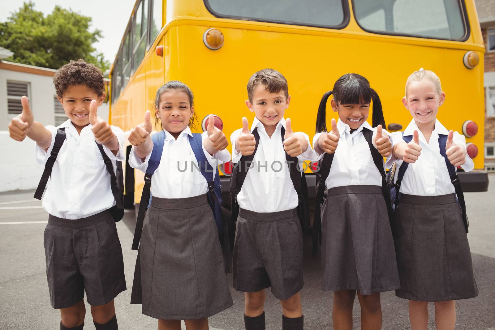 Cute schoolchildren smiling at camera by the school bus outside the elementary school