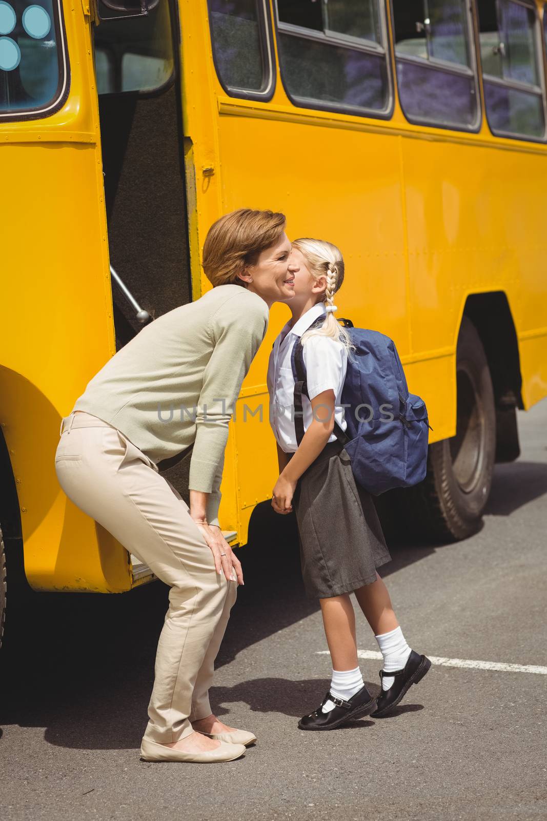 Mother kissing her daughter by school bus outside the elementary school