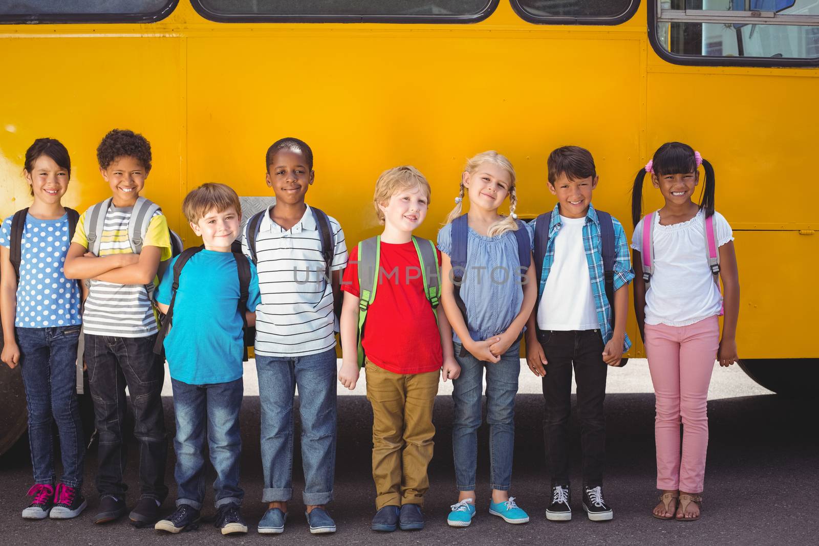 Cute pupils smiling at camera by the school bus outside the elementary school