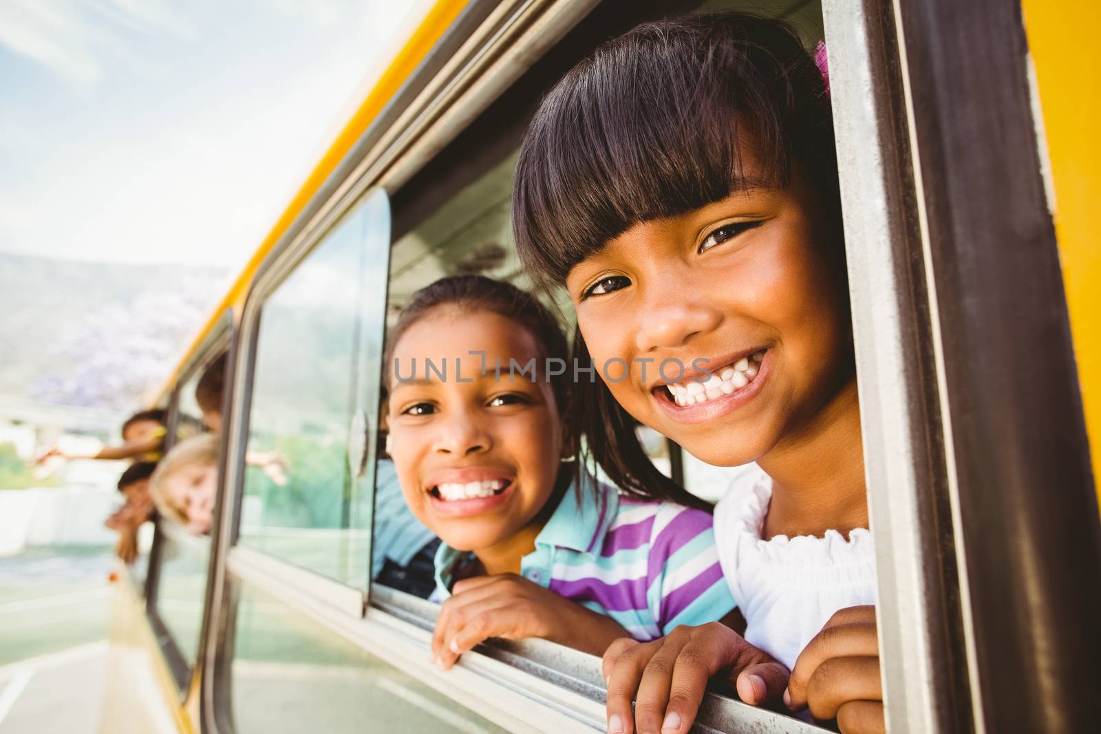 Cute pupils smiling at camera in the school bus outside the elementary school