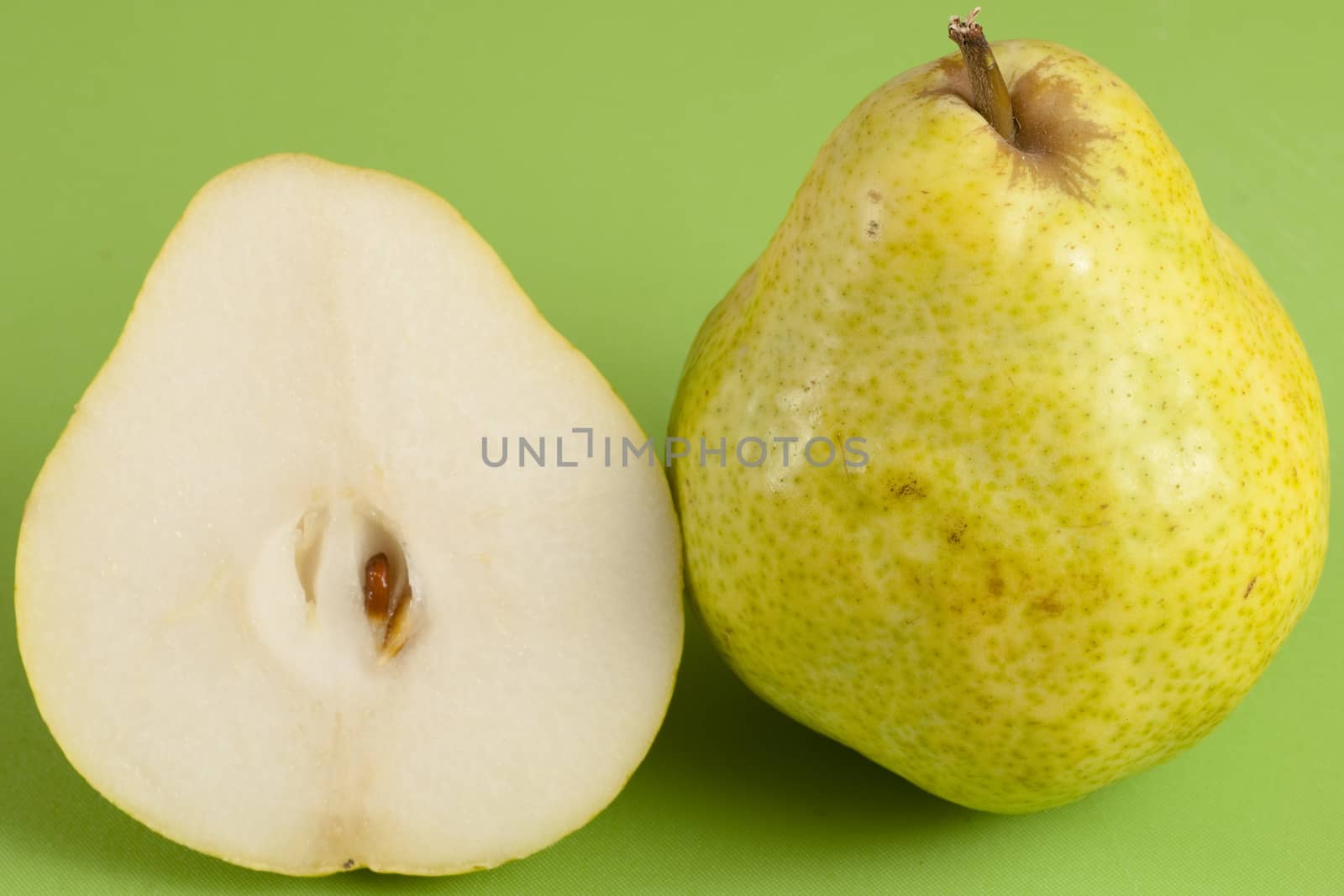 green pear cut in half on a green floor and a whole pear