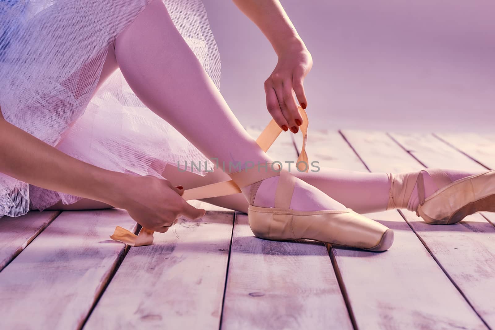 Professional ballerina putting on her ballet shoes on the wooden floor on a pink background. feet close-up