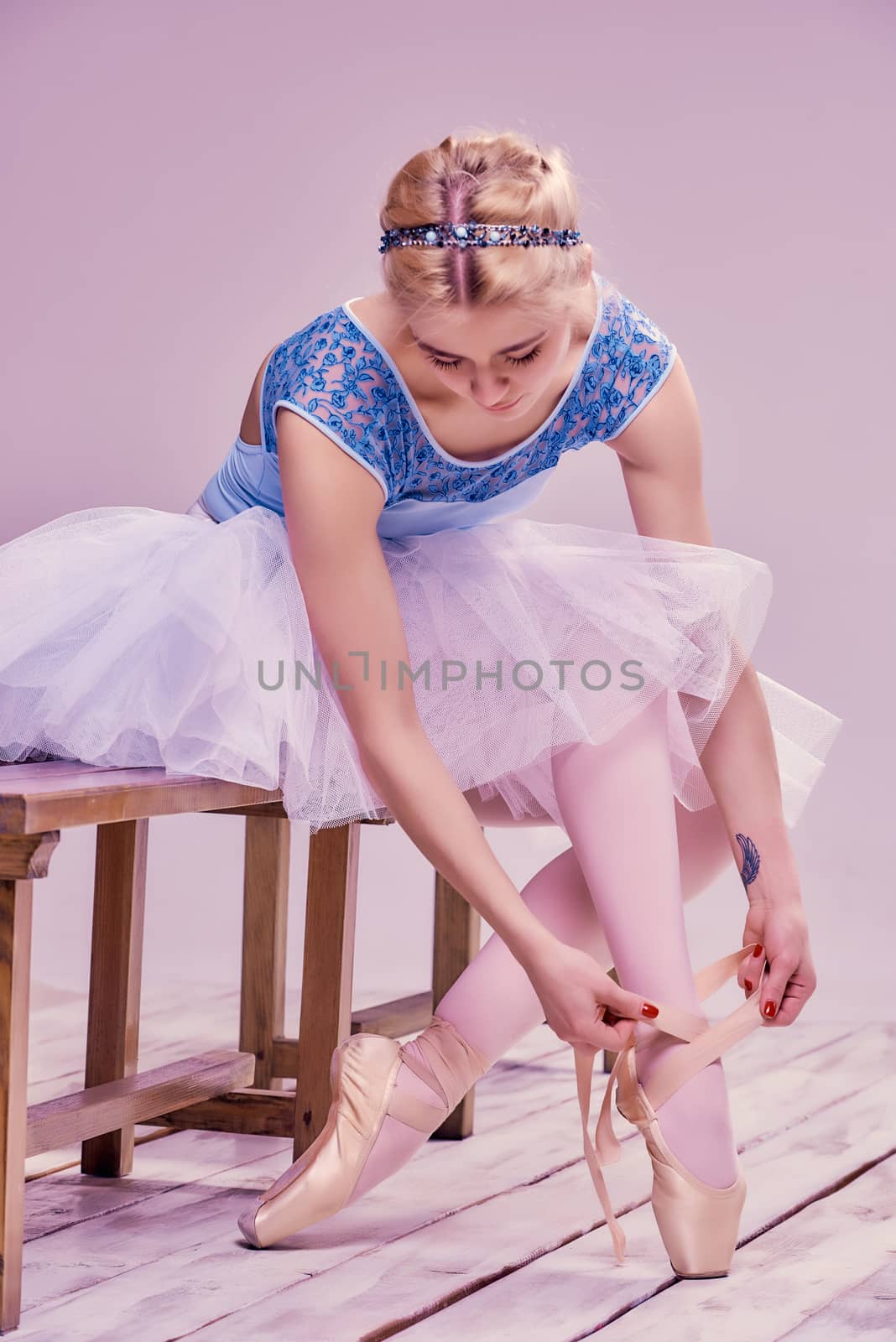 Professional ballerina putting on her ballet shoes on the wooden floor on a pink background