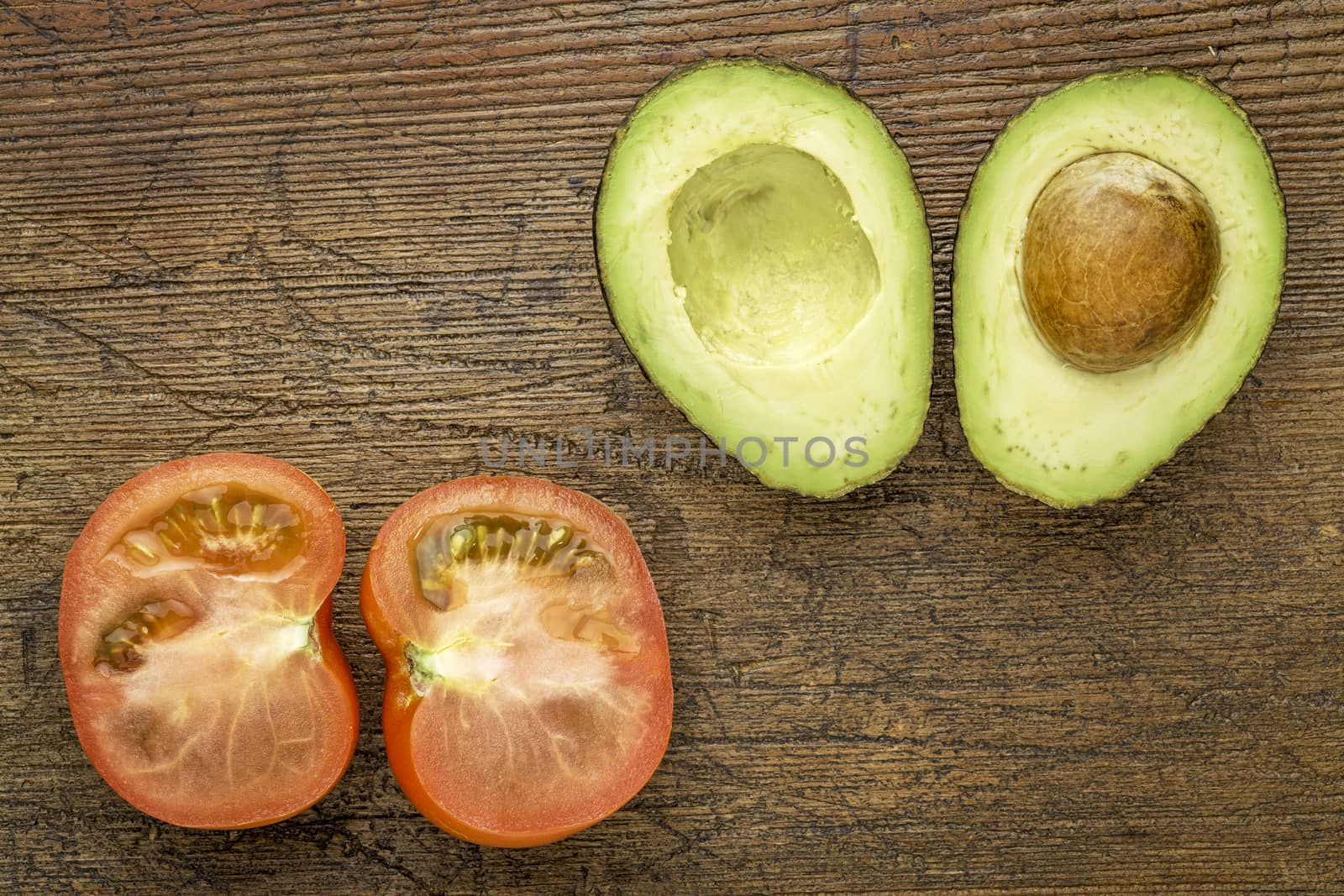 avocado and tomato cut in half on a grunge wood with a copy space