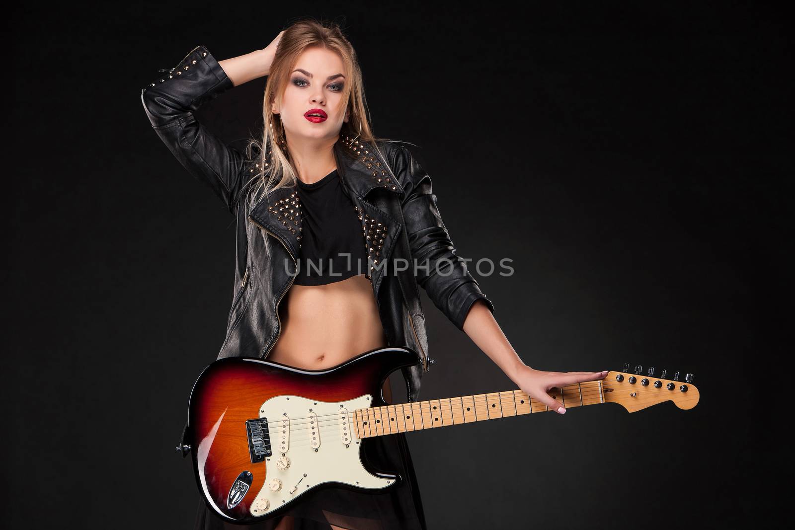 Beautiful blonde girl playing guitar in rock style on a black background