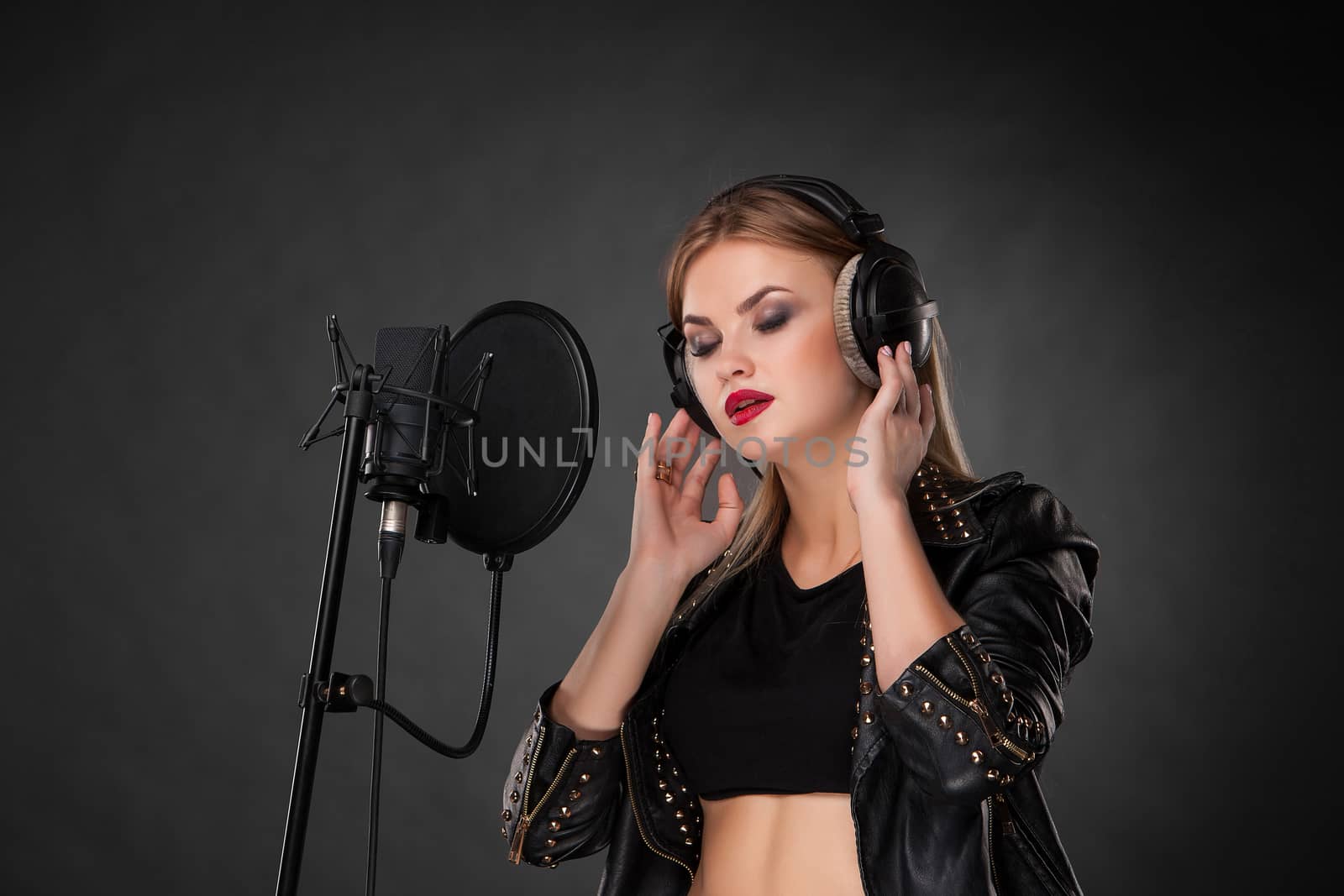Portrait of a beautiful woman singing into microphone with headphones in studio on black background by master1305