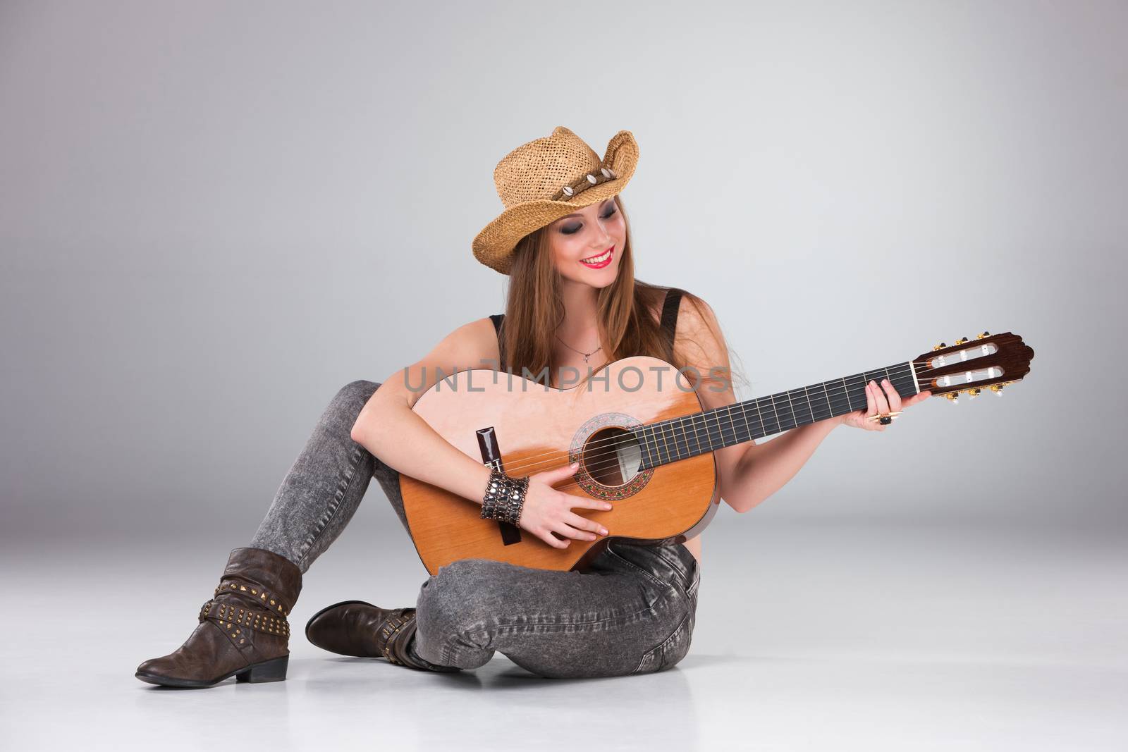 The beautiful girl in a cowboy's hat playing acoustic guitar on a gray background