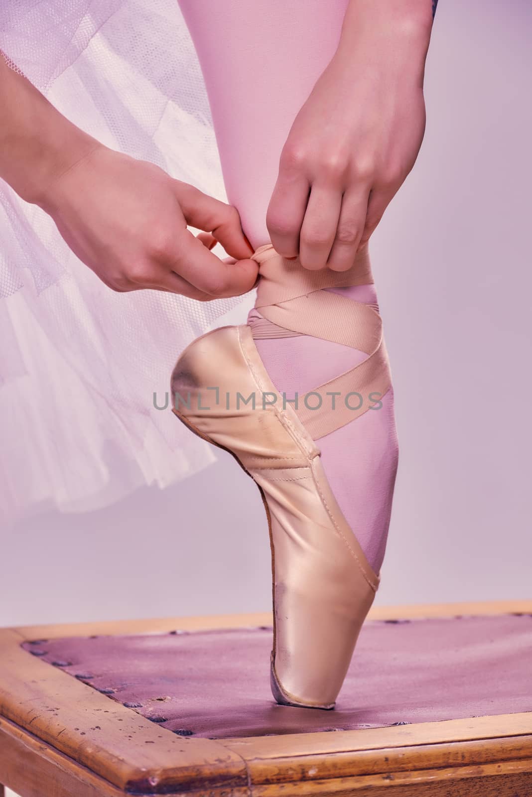 Professional ballerina putting on her ballet shoes.on the  wooden chair on a pink background. feet close-up
