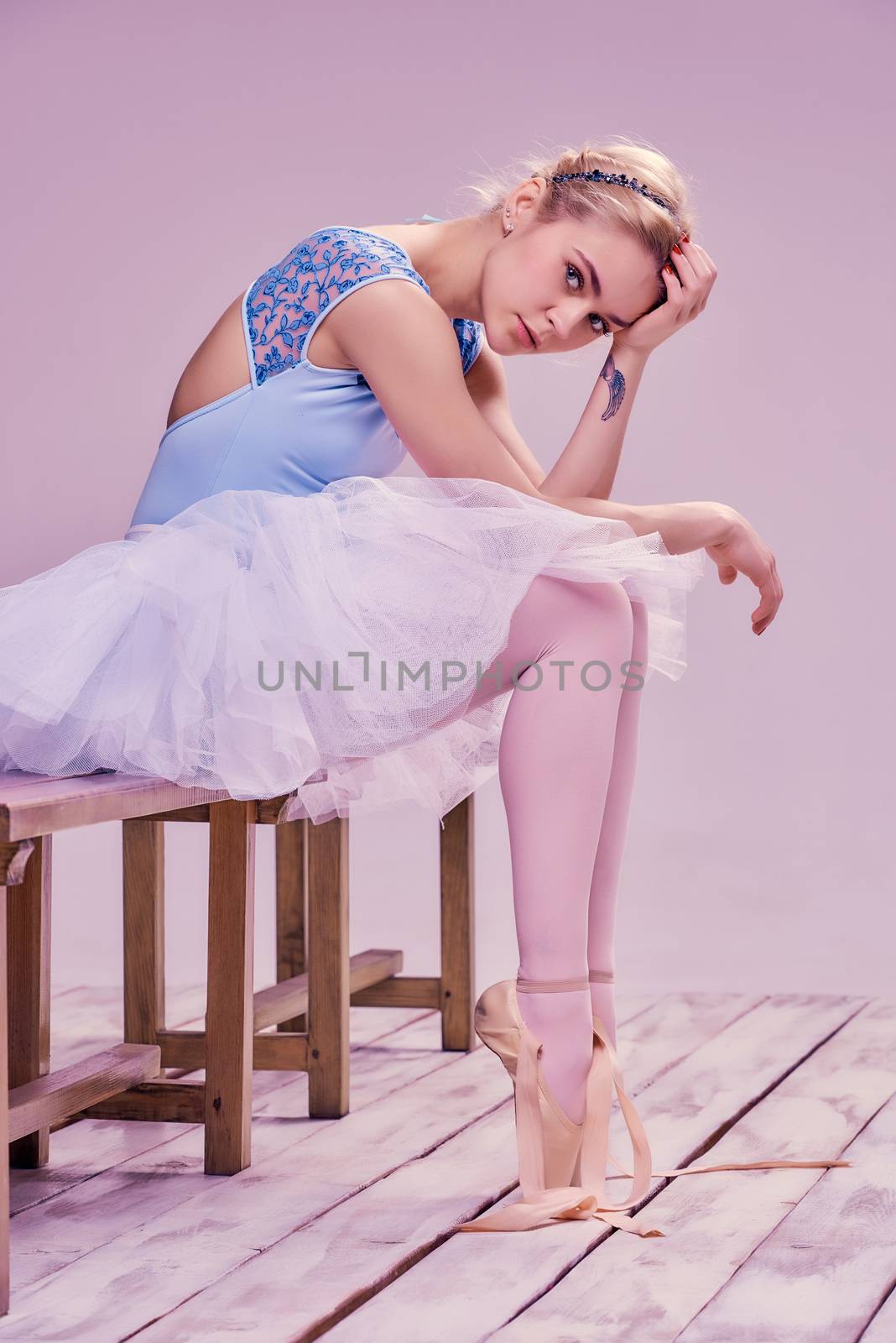 Tired ballet dancer sitting on the wooden floor on a pink background