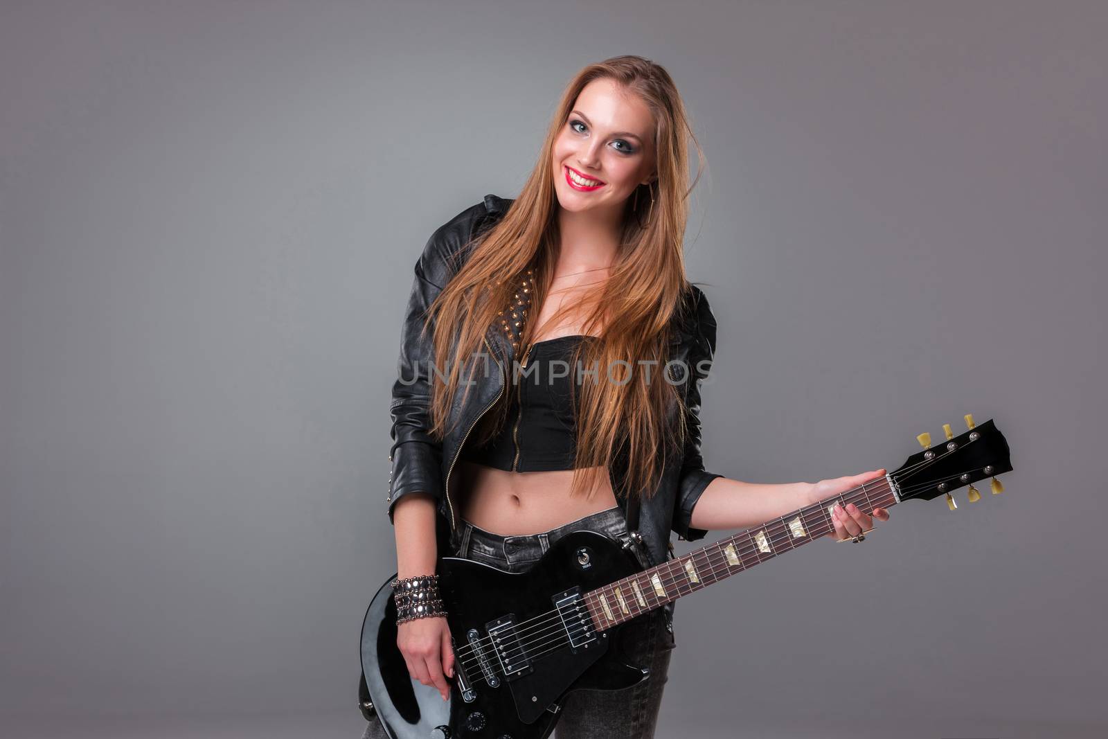 Beautiful girl  with long hair playing guitar in rock style on a gray background