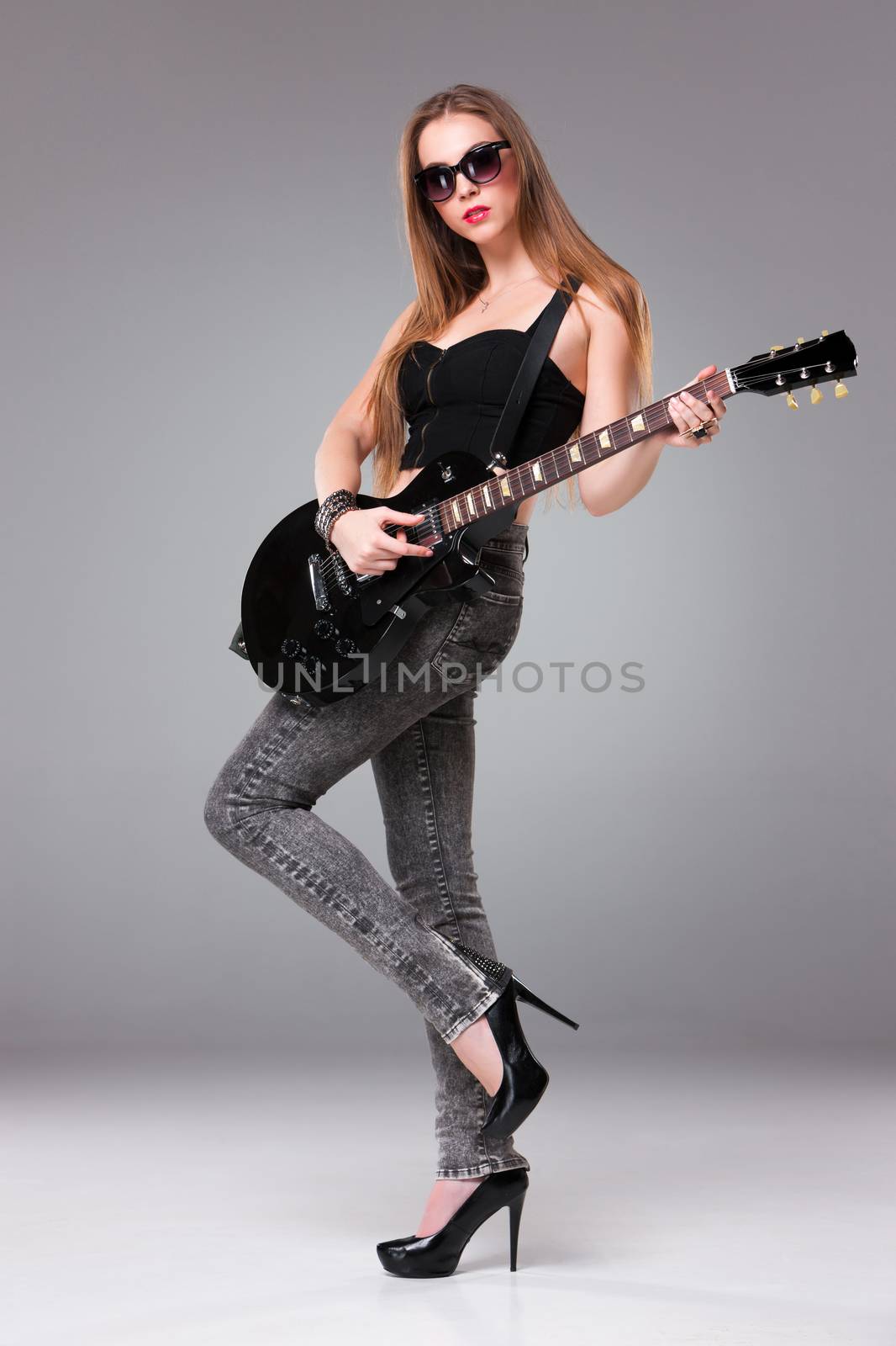 Beautiful girl with sunglasses playing guitar in rock style on a gray background