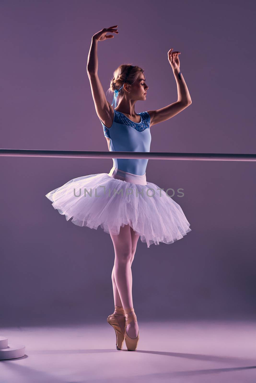 classic ballet dancer in white tutu at ballet barre on a lilac background