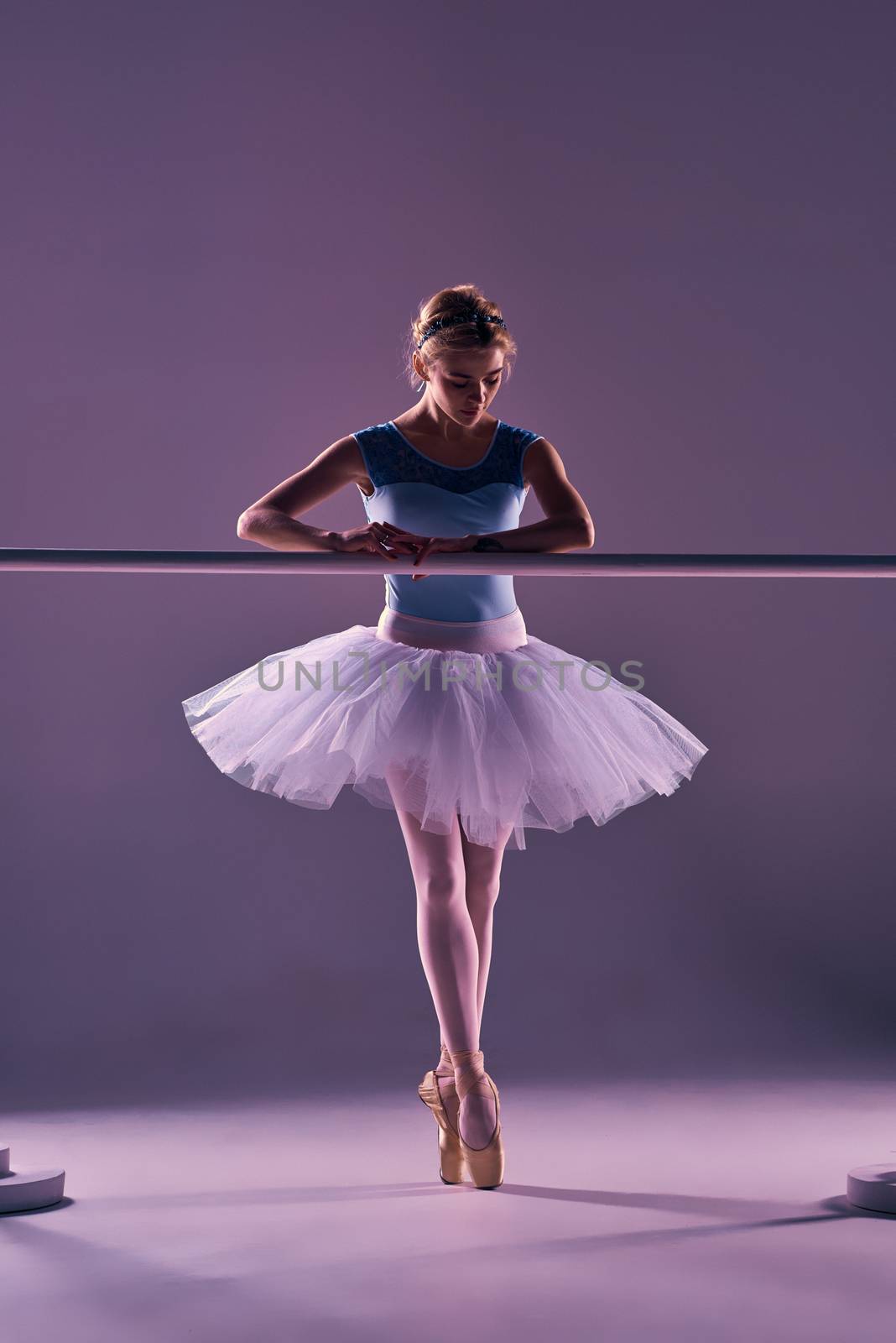 classic ballet dancer in white tutu at ballet barre on a lilac background