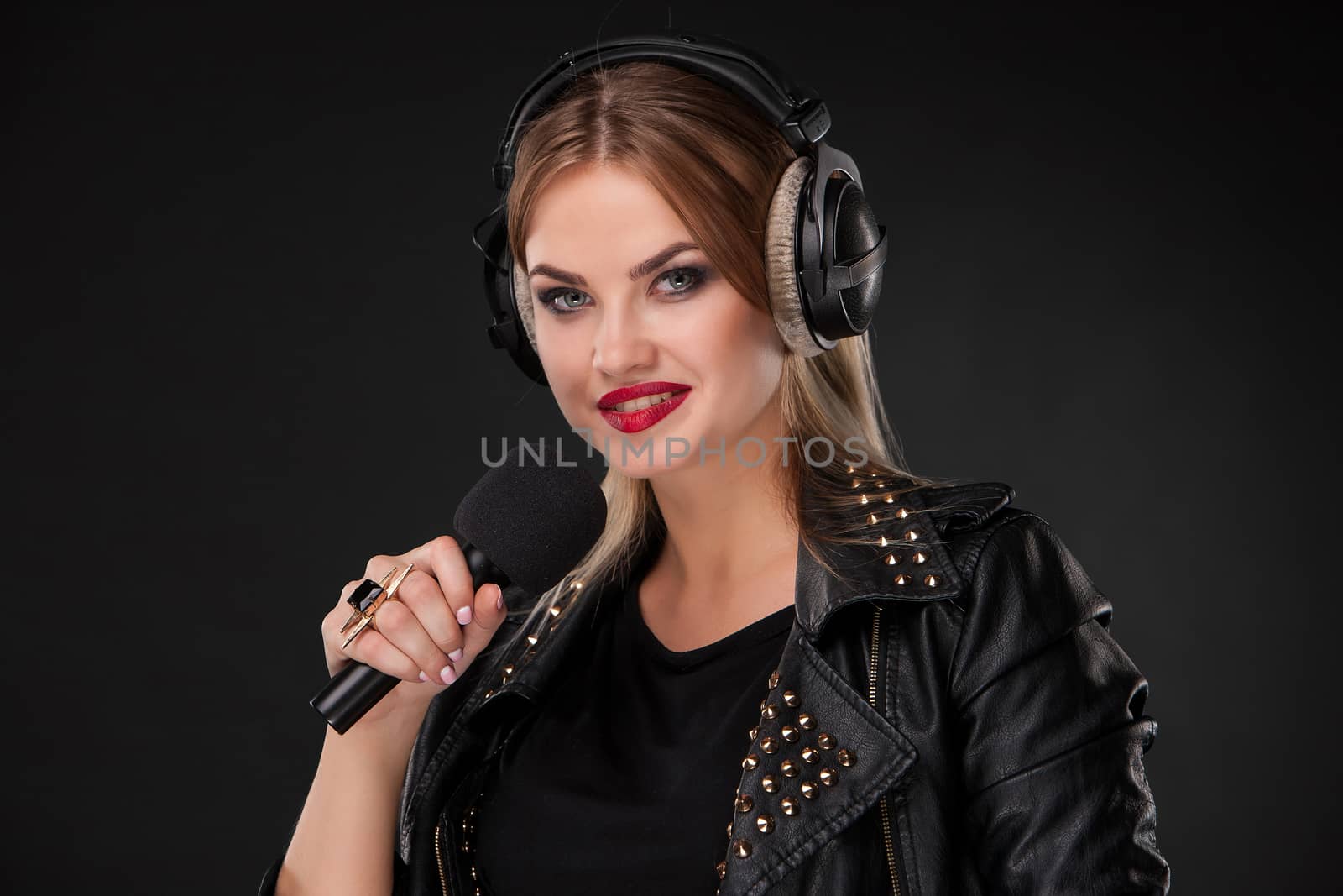 Portrait of a beautiful blonde young woman singing into microphone with headphones in studio on black background