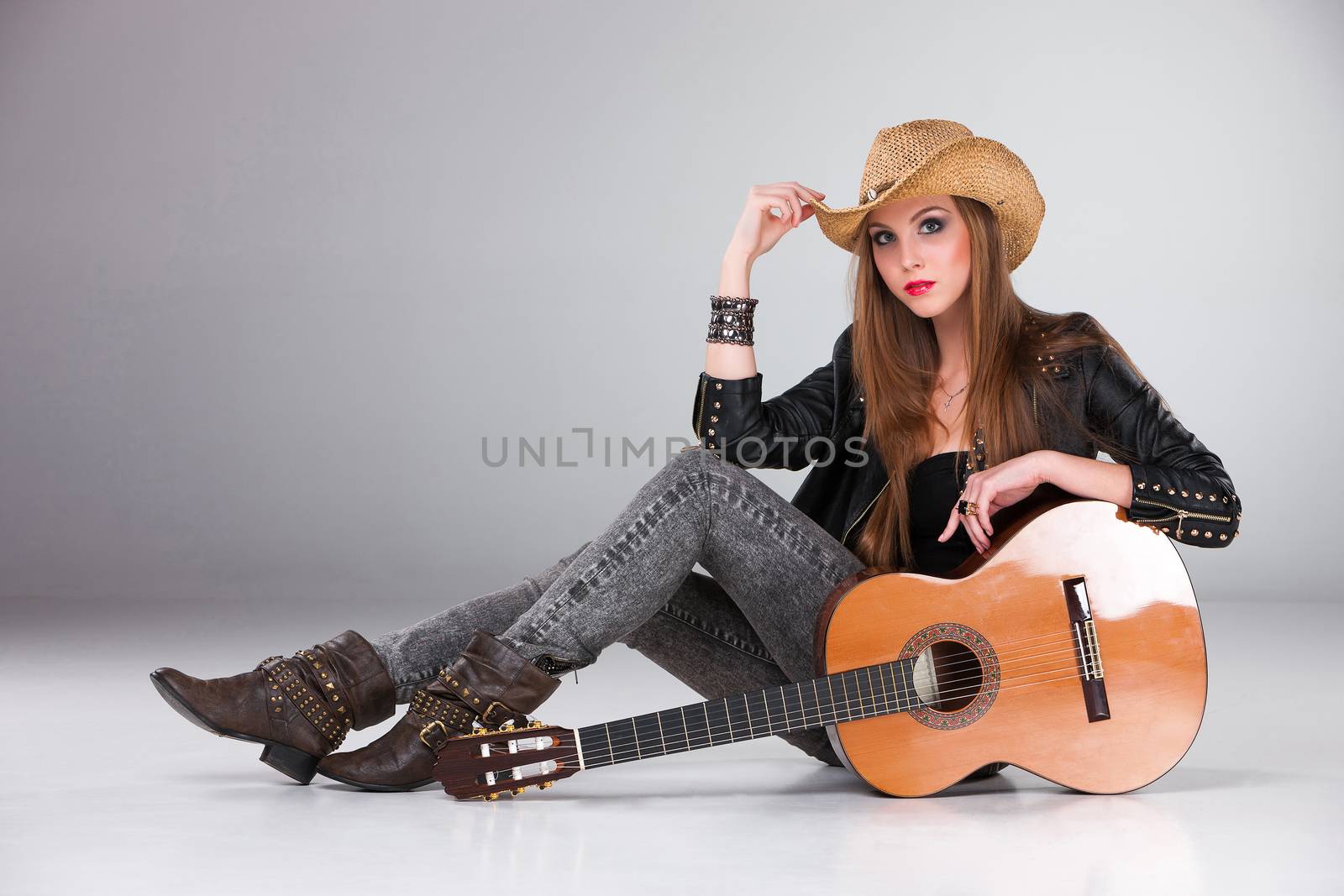 The beautiful girl in a cowboy's hat  and acoustic guitar on a gray background