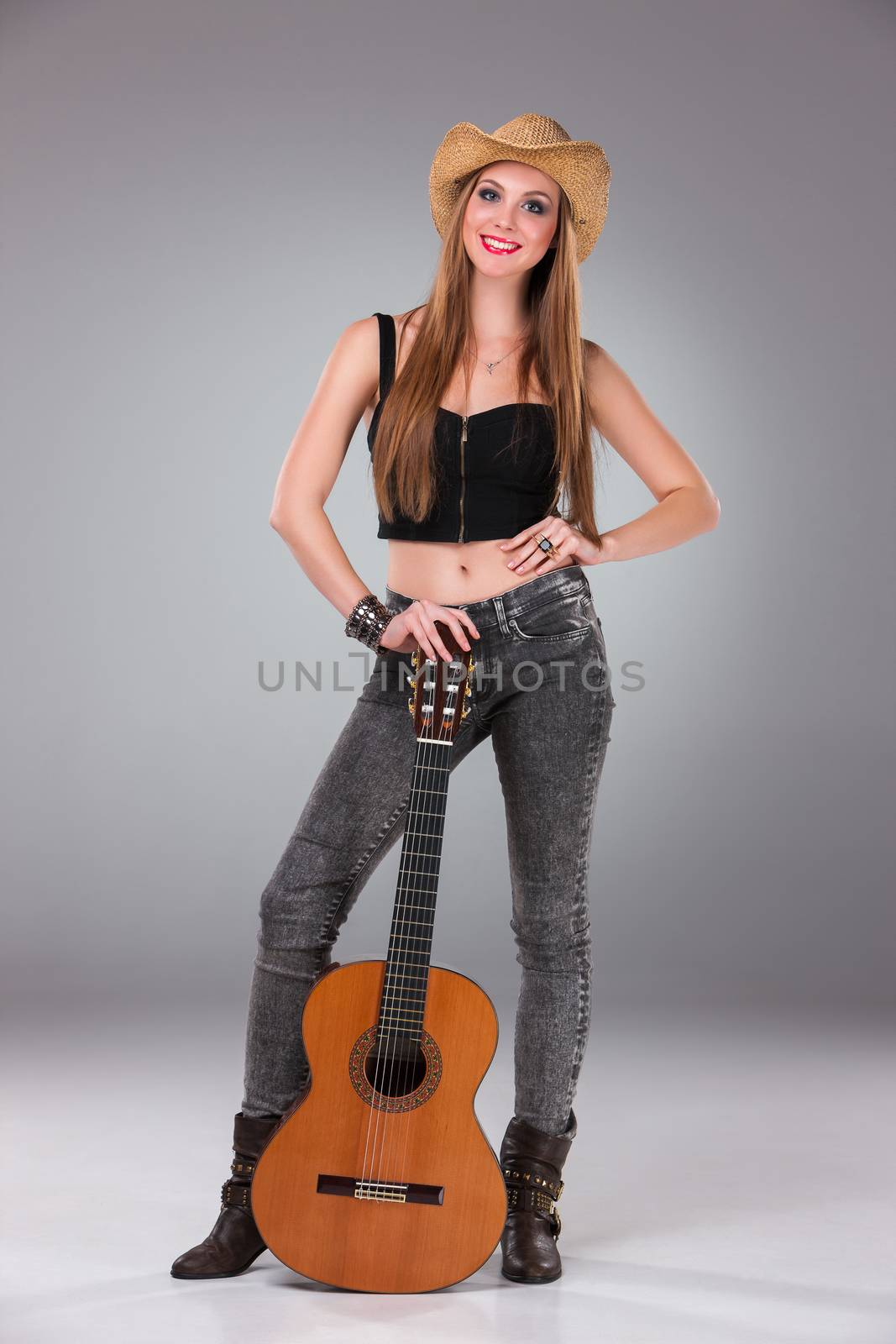 The beautiful girl in a cowboy's hat and acoustic guitar on a gray background