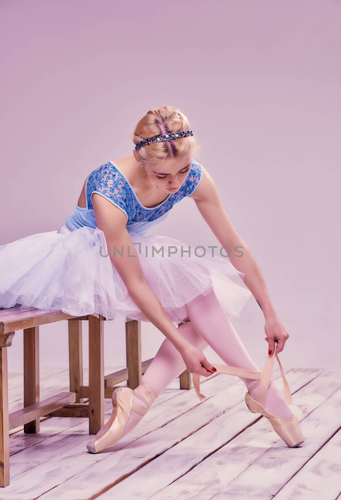 Professional ballerina putting on her ballet shoes on the wooden floor on a pink background