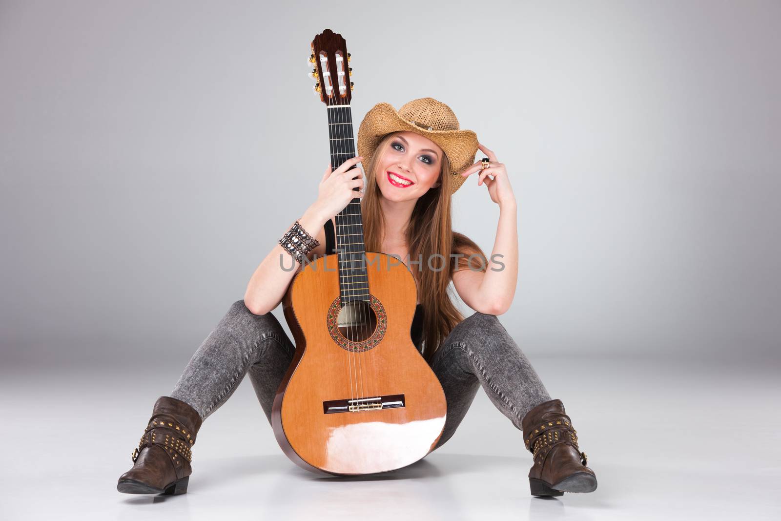 The beautiful girl in a cowboy's hat  and acoustic guitar on a gray background