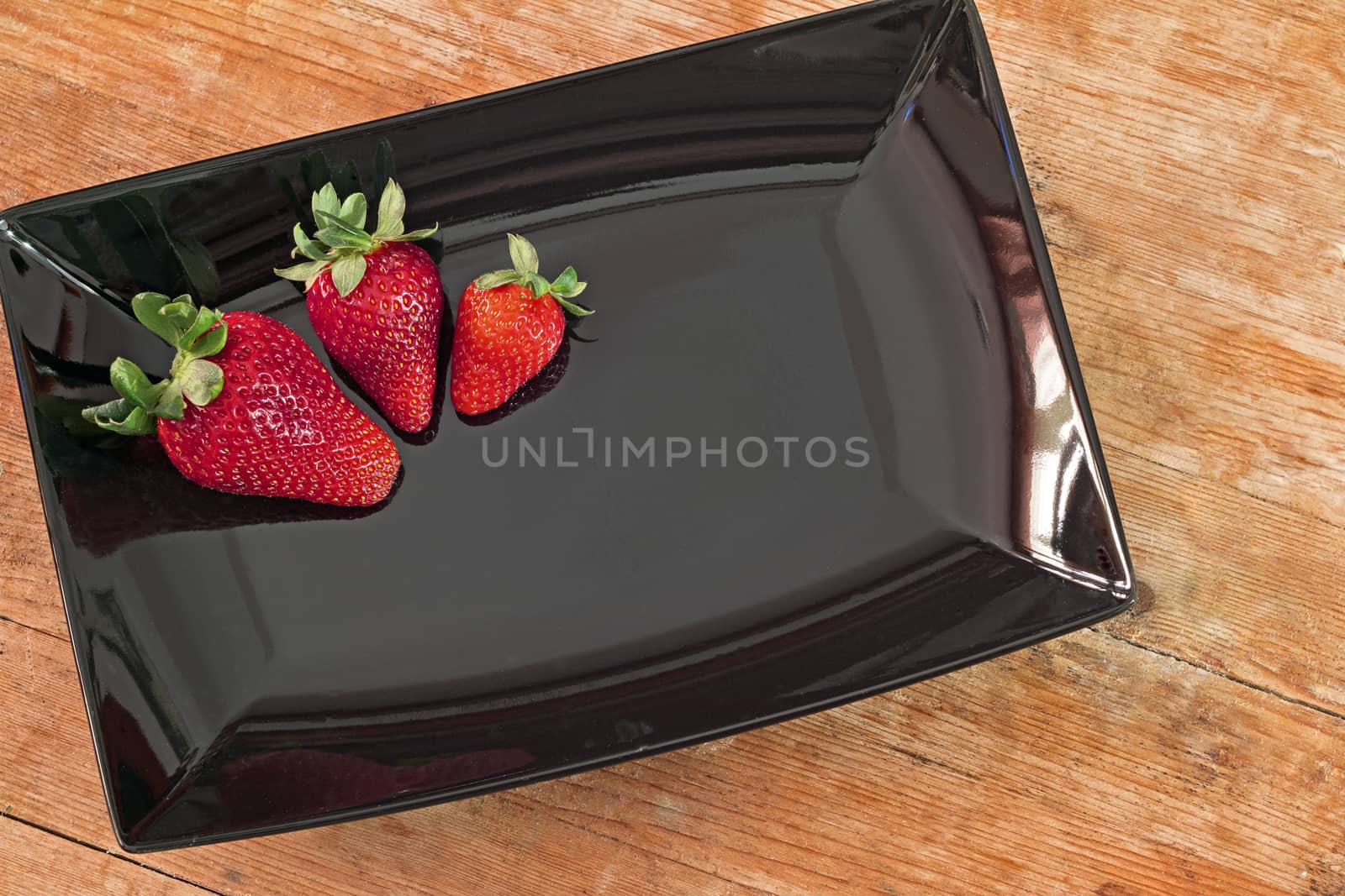 three red strawberries in a black plate and wooden base