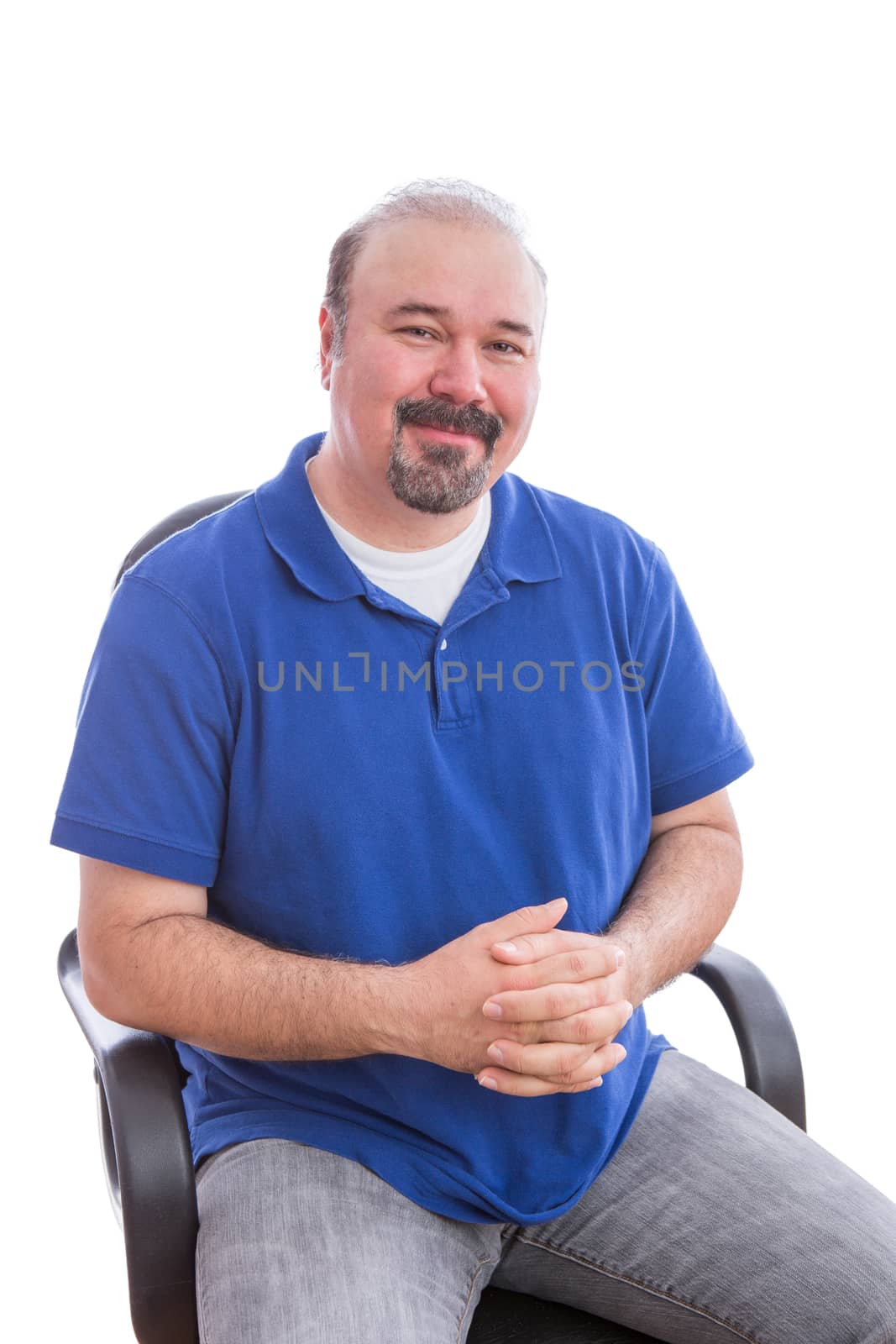 Close up Happy Bearded Adult Man in Blue Shirt Sitting on a Single Chair with Hands Crossed Over her Belly, Looking at the Camera with Admiration. Isolated on White Background.