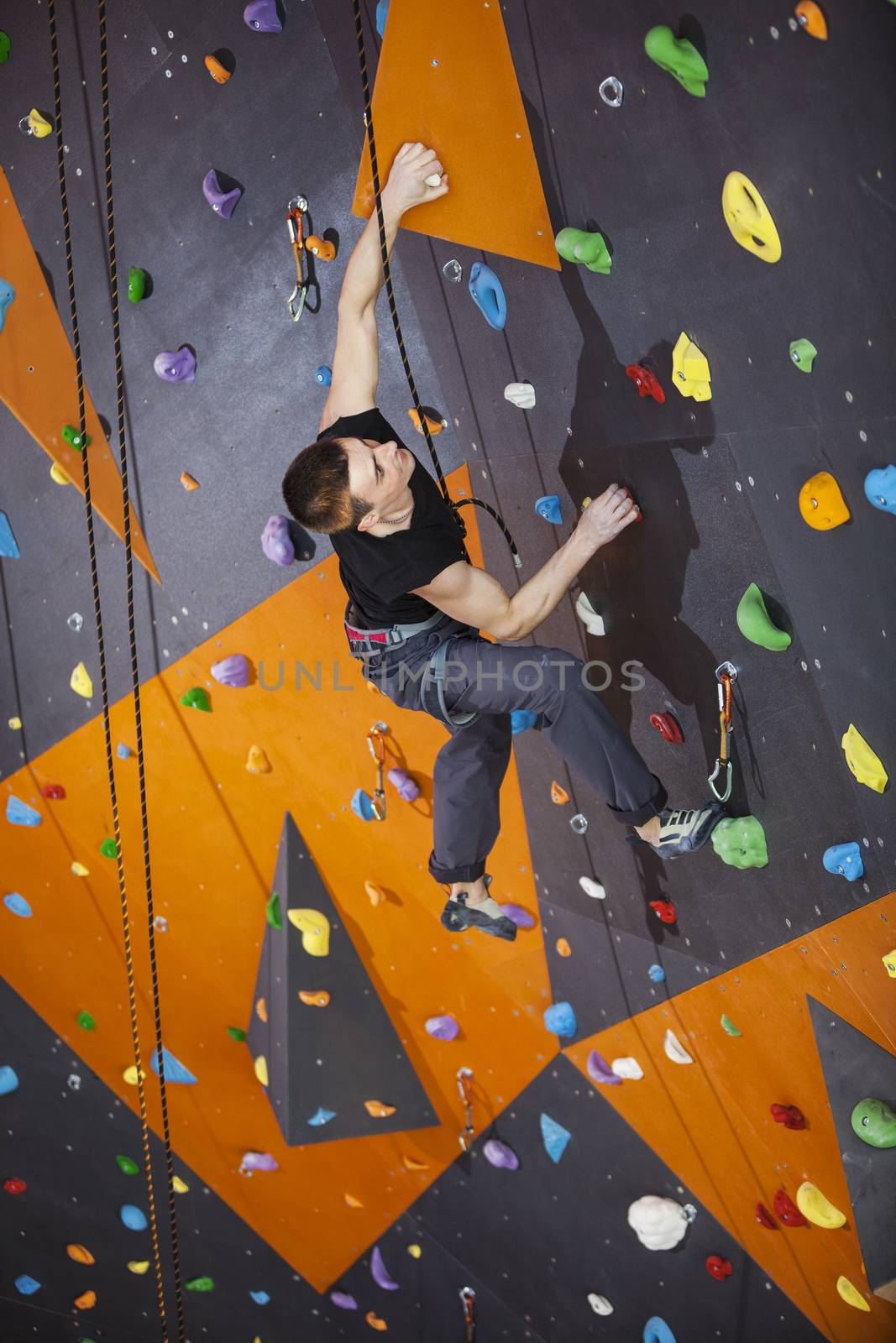 Young man practicing top rope climbing in indoor climbing gym