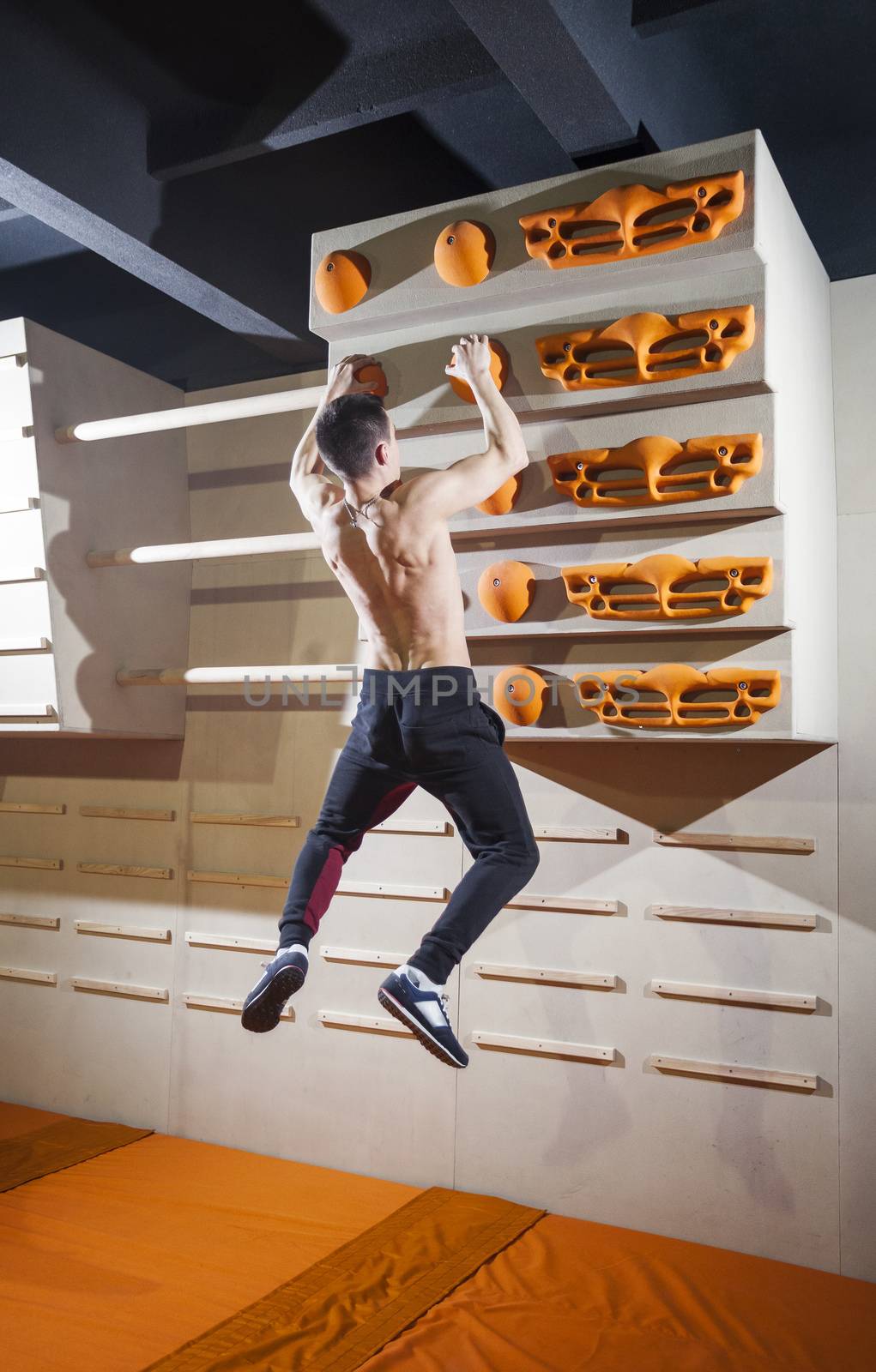 Young man practicing rock-climbing in climbing gym by photobac