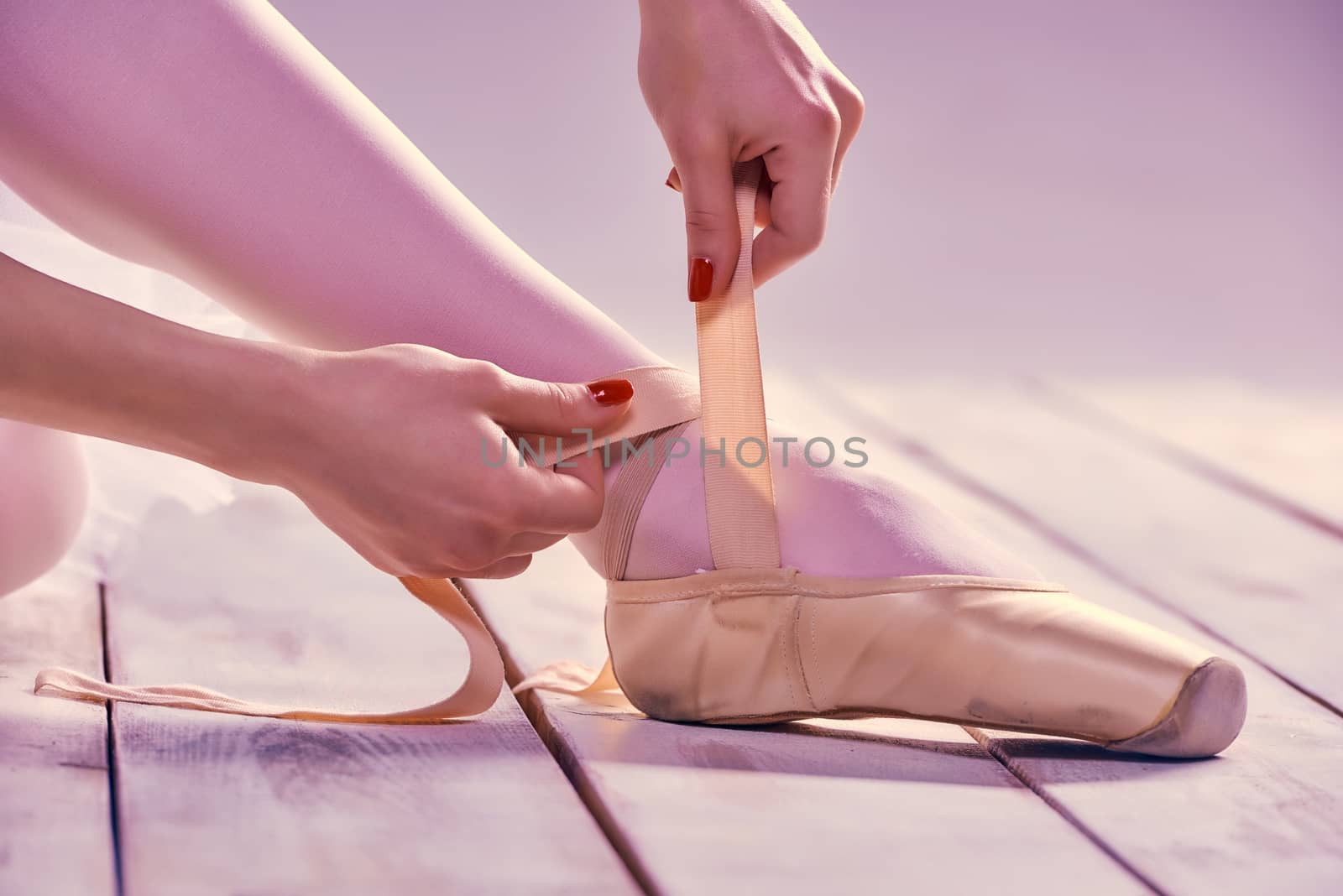 Professional ballerina putting on her ballet shoes on the wooden floor on a pink background. feet close-up