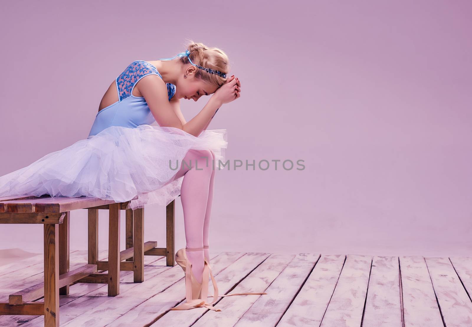 Tired ballet dancer sitting on the wooden floor on a pink background