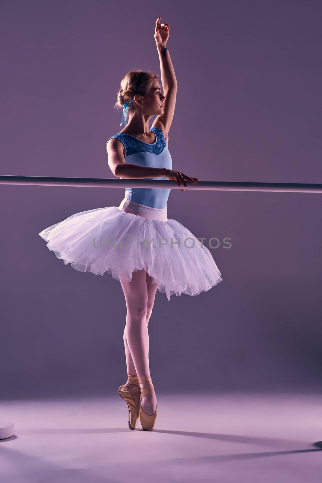 classic ballet dancer in white tutu at ballet barre on a lilac background