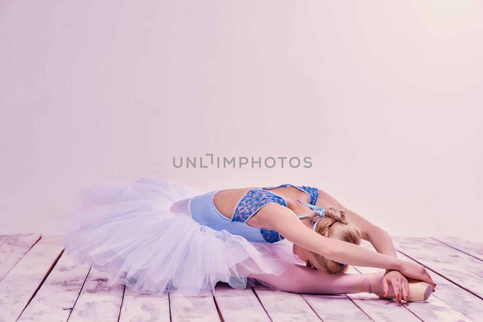 Tired ballet dancer lying on the wooden floor on a pink background