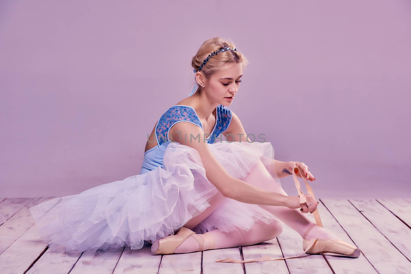 Professional ballerina putting on her ballet shoes on the wooden floor on a pink background