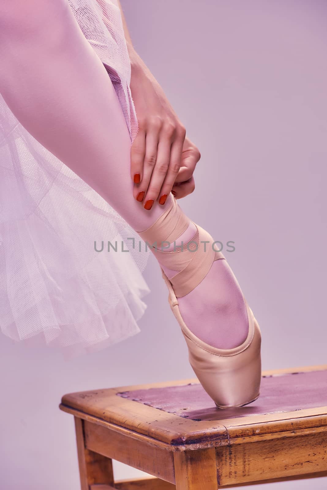 Professional ballerina putting on her ballet shoes.on the  wooden chair on a pink background. feet close-up