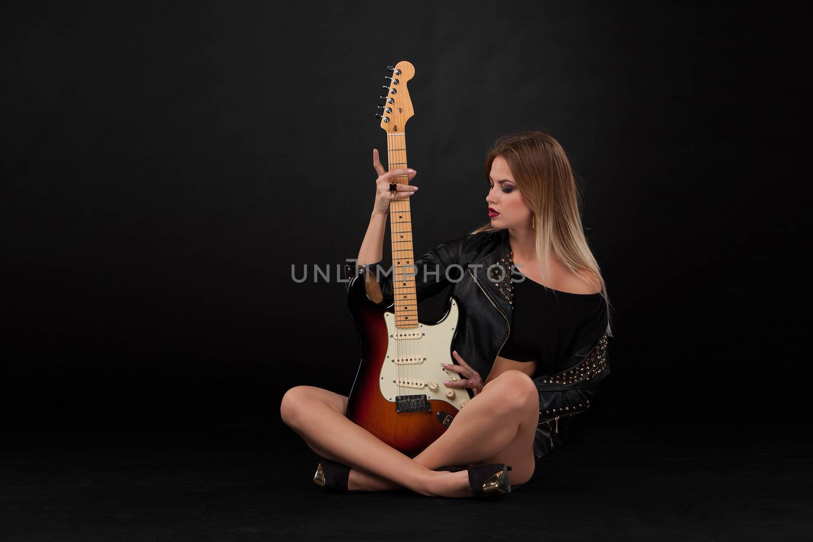 Beautiful blonde girl and guitar in rock style on a black background