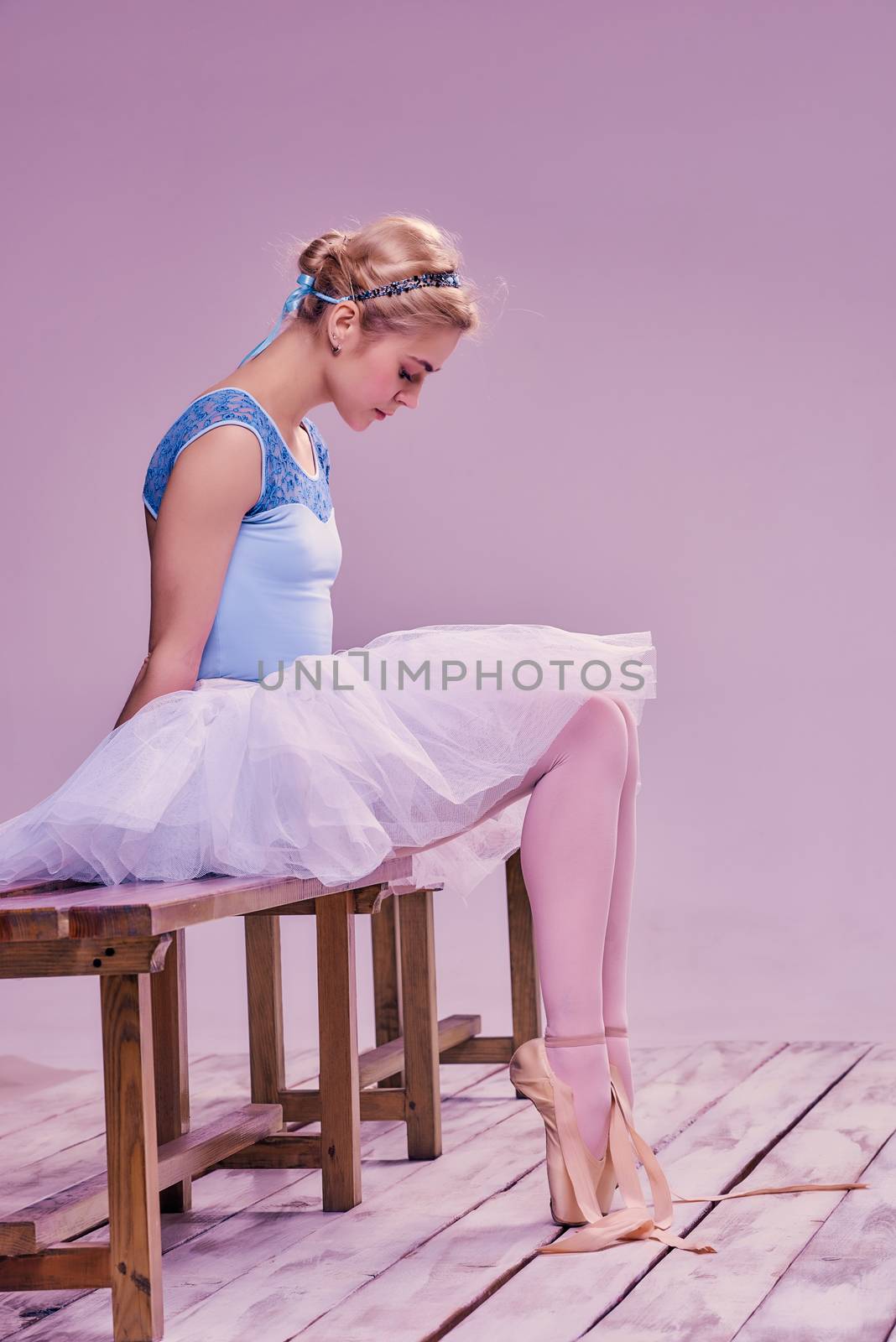 Tired ballet dancer sitting on the wooden floor on a pink background