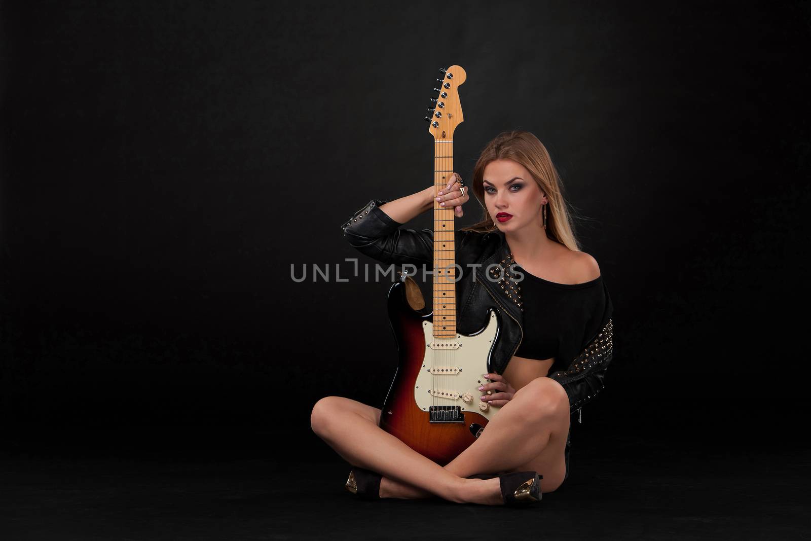 Beautiful blonde girl and guitar in rock style on a black background