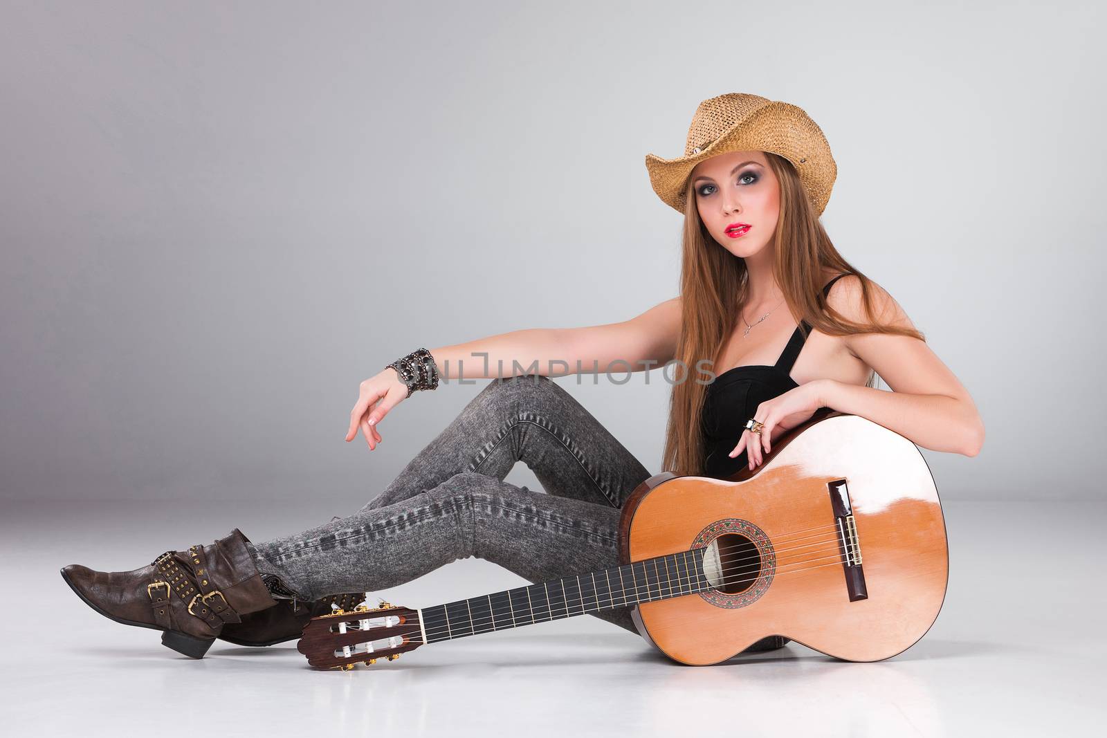 The beautiful girl in a cowboy's hat  and acoustic guitar on a gray background