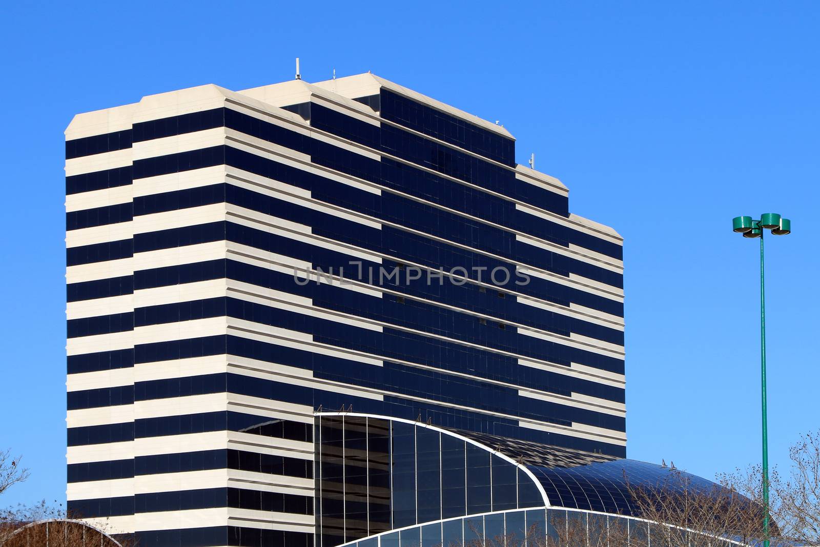 Beautiful modern office building set against a blue sky.  The building also has a lower level atrium area visible.  The building is built of glass and stucco over a steel frame.
