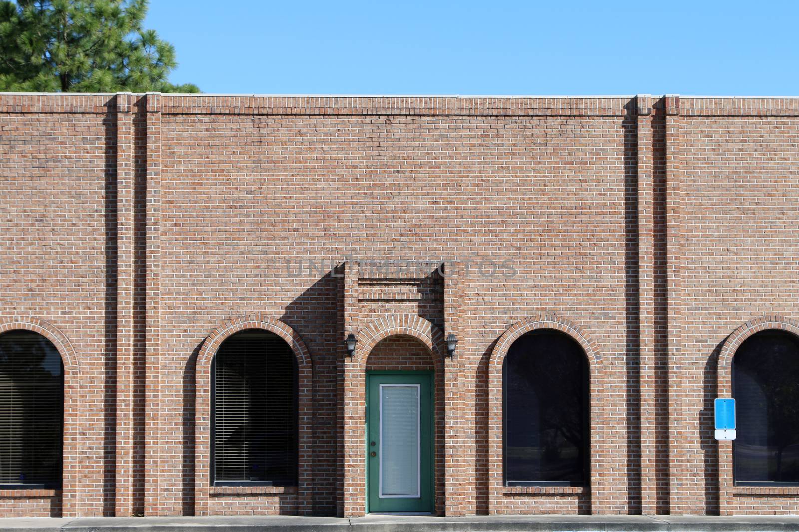 Unoccupied generic store front, business or professional office space in a contemporary strip mall. Brown brick with dark tinted windows with arches.