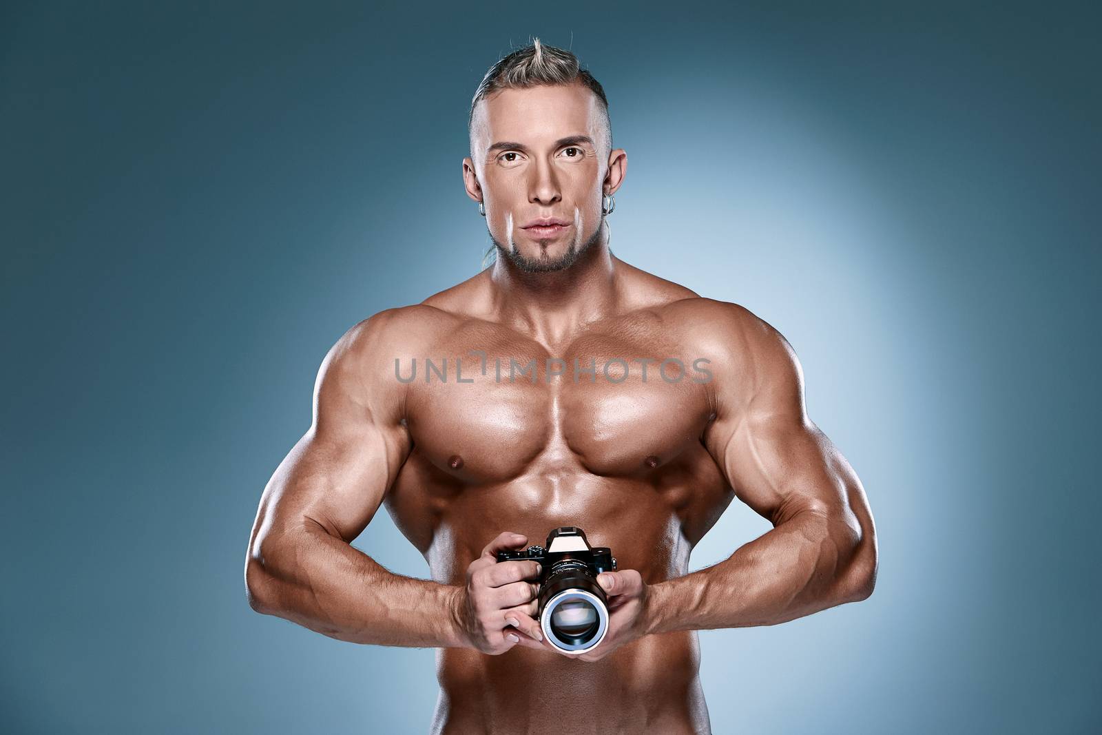 Attractive male body builder as photograph holding a camera on blue background