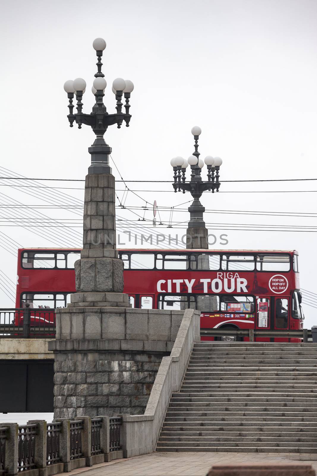 RIGA, LATVIA - MARCH 29, 2015: Red double-decker city sightseeing bus between two lanterns of Stone bridge.