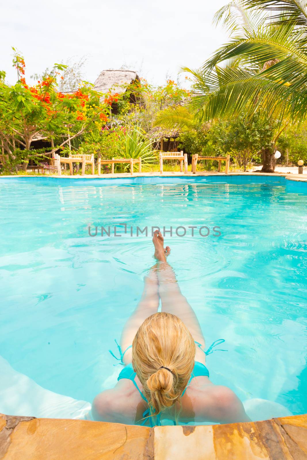 Beautiful Caucasian woman floating in turquoise blue swimming pool.