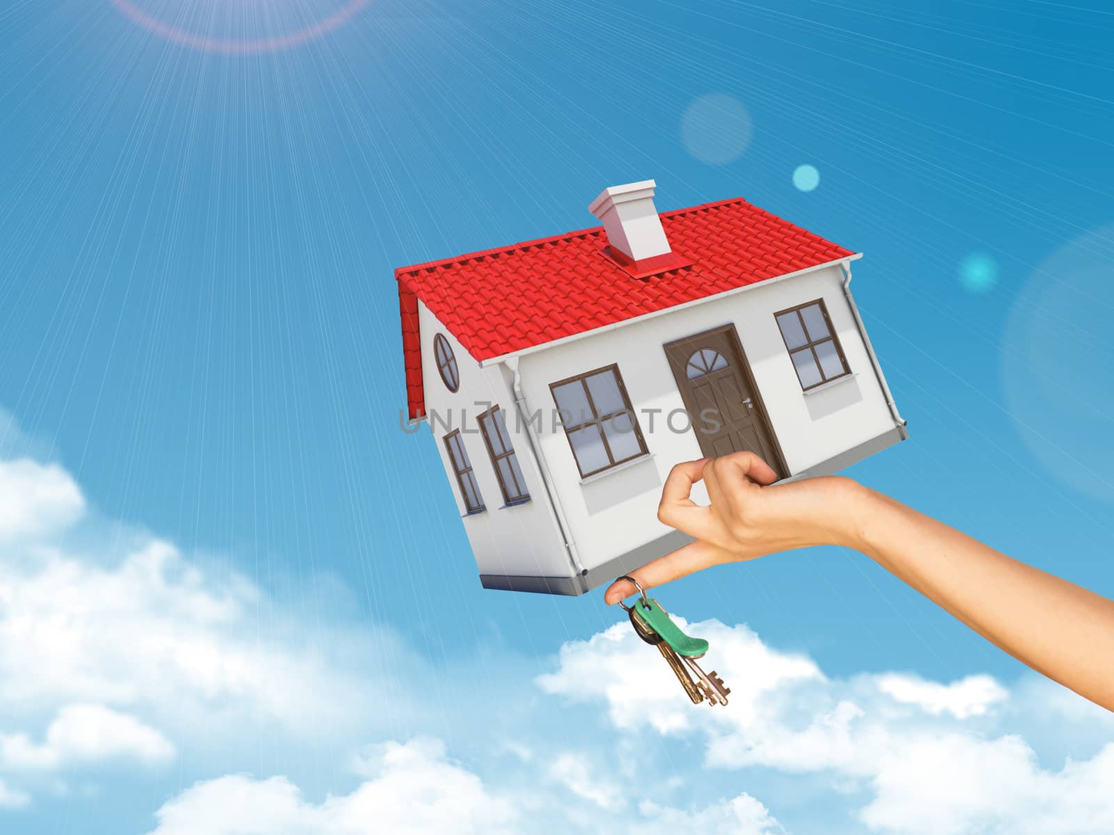 House and keys in womans left hand under clouds on blue sky background 