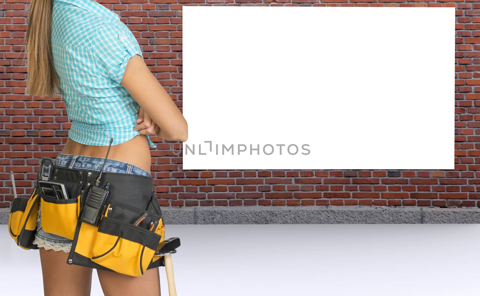 Young woman with crossed arms and tool belt and blank drawing paper, rear view. Wall brick texture background